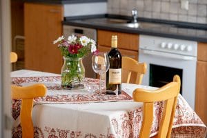 Eßtisch mit Weingläßern, Wein und Blumenstrauß im Hintergrund Wohnküche der Wohnung Kamille der Josenmühle