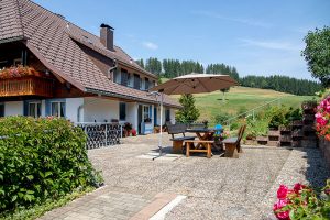 Großzügige Terrasse mit Holzbänken und Tisch und großem Sonneschirm - Josenmuehle